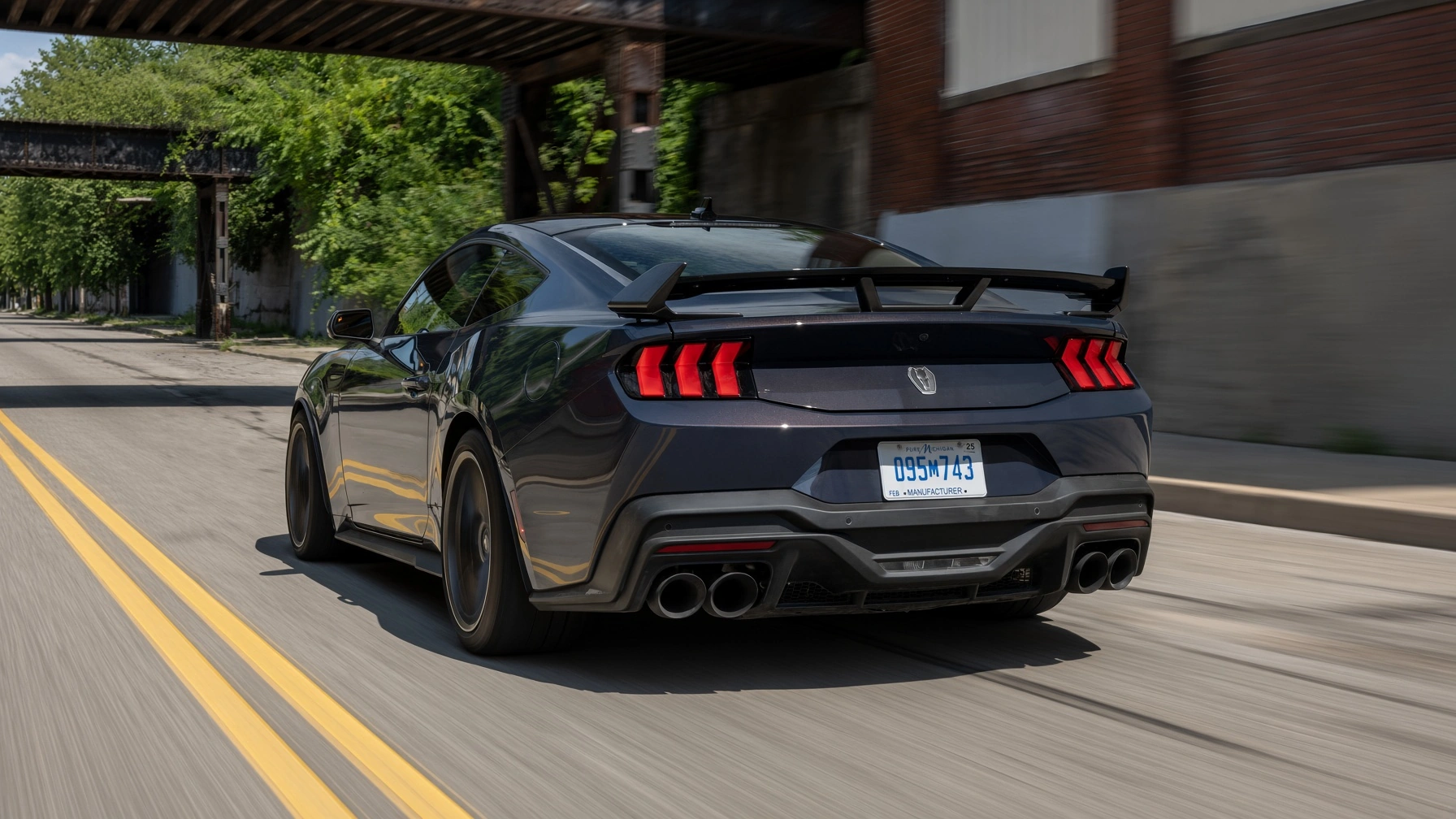 Ford Mustang Dark Horse gris visto desde atrás en movimiento, con alerón y escape de cuatro salidas